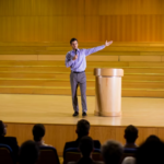 A featured image featuring a speaker showcasing his public speaking techniques before an audience